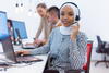 a woman wearing a headset on a call sitting at a table using a laptop computer